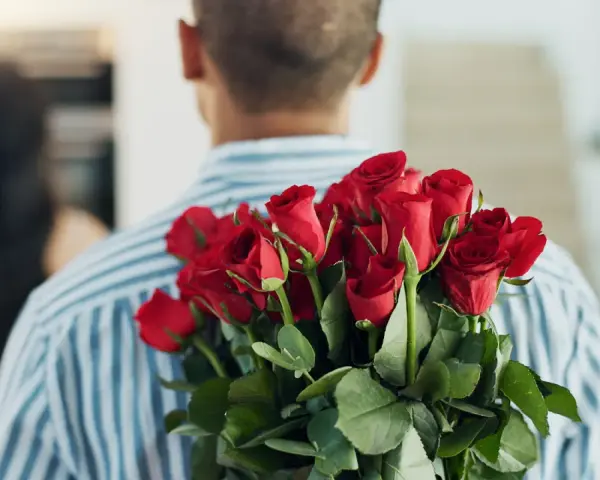 Mężczyzna z bukietem czerwonych róż za plecami. 15 roz co oznacza? Miłość, namiętność, romantyzm.