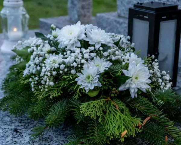 Białe kompozycje z chryzantem i iglastymi gałązkami na grobie, symbol pamięci na Wszystkich Świętych.