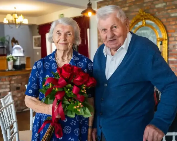 Para świętuje 70 rocznicę ślubu. Ona trzyma bukiet czerwonych róż, on stoi obok.