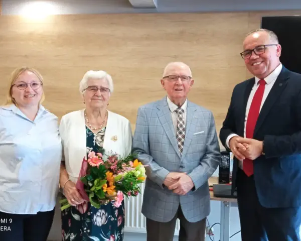 Para świętuje 65 rocznicę ślubu. Jubilaci z bukietem kwiatów, obok nich młodsza kobieta i mężczyzna w garniturze.
