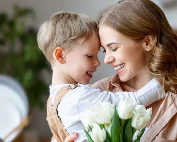 Uśmiechnięta mama i synek przytulają się, trzymając bukiet białych tulipanów. Idealny obrazek na Dzień Mamy.