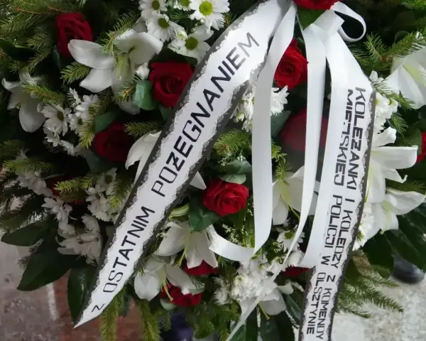 Wieniec pogrzebowy z białymi liliami i czerwonymi różami. Napis na szarfie: "Z ostatnim pożegnaniem od koleżanki i kolegów z Komendy Miejskiej Policji w Olsztynie".