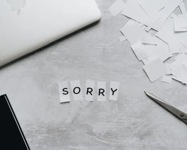 Litery wycięte z papieru układają się w napis "SORRY". Obok leżą nożyczki i stos białych skrawków, jakby ktoś tworzył piękny list na przeprosiny.
