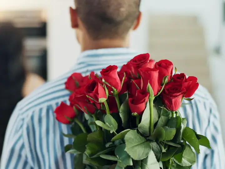 Mężczyzna z bukietem czerwonych róż za plecami. 15 roz co oznacza? Miłość, namiętność, romantyzm.