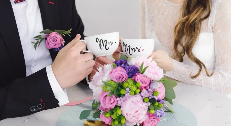 Para świętuje 4 rocznicę ślubu, trzymając kubki "Mr." i "Mrs." na tle bukietu kwiatów.