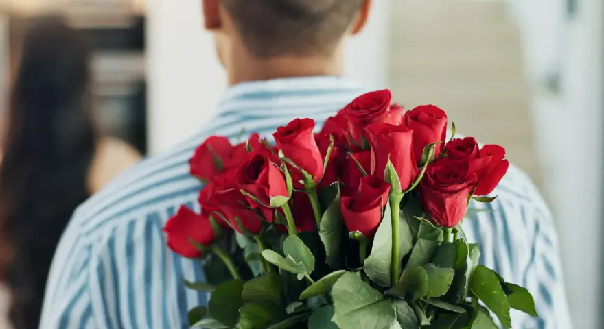 Mężczyzna z bukietem czerwonych róż za plecami. 15 roz co oznacza? Miłość, namiętność, romantyzm.