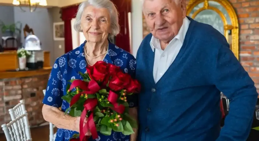 Para świętuje 70 rocznicę ślubu. Ona trzyma bukiet czerwonych róż, on stoi obok.