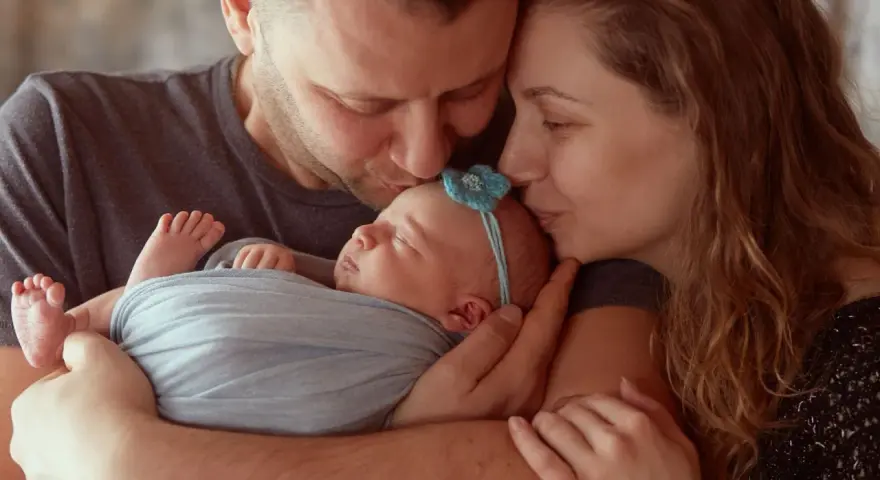Rodzice całują śpiące maleństwo. Serdeczne gratulacje z okazji narodzin córeczki!