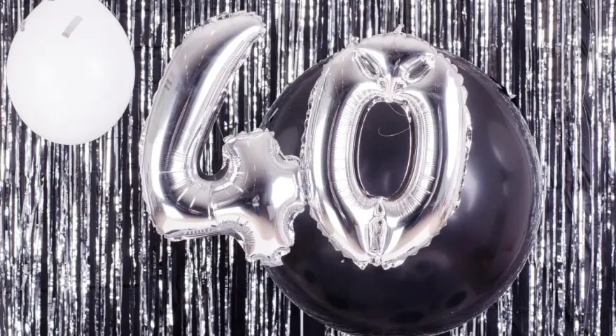 Srebrne balony z cyfrą 40 i biały balon na tle błyszczącej kurtyny. Idealne na zabawy na 40 urodziny!