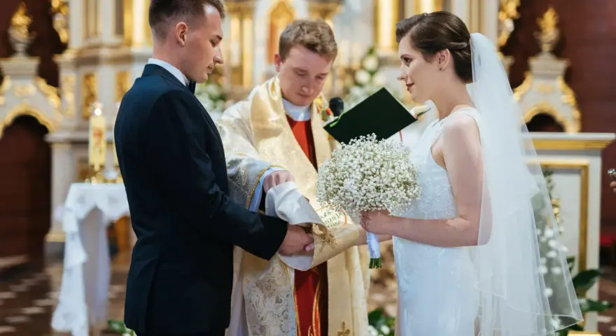 Panna młoda w welonie i z bukietem, pan młody w garniturze, podczas ceremonii ślubnej w kościele.