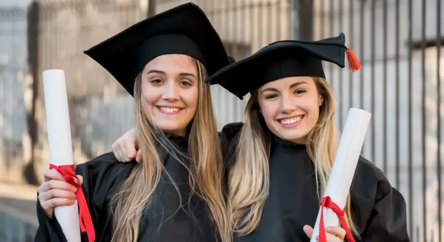 Dwie uśmiechnięte absolwentki medycyny w togach i biretach trzymają dyplomy. Gratulacje z okazji ukończenia studiów medycznych!