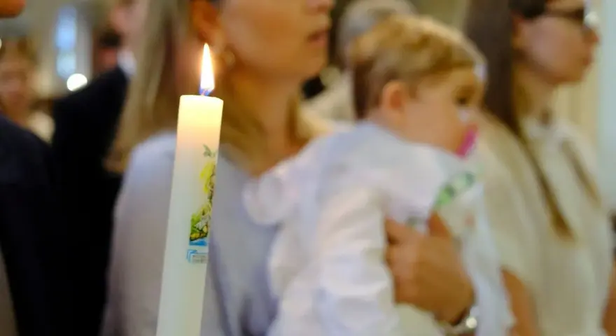 Chrzest dziecka. Czy świadek chrztu musi mieć zaświadczenie? Płonąca świeca chrzcielna w dłoniach.