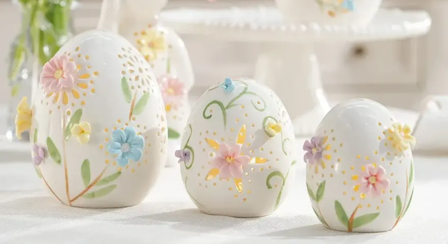 Białe, ceramiczne jajka z pastelowymi kwiatami i listkami, ozdobione ażurowymi wzorami. Te piękne symbole wielkanocne tworzą magiczną atmosferę.