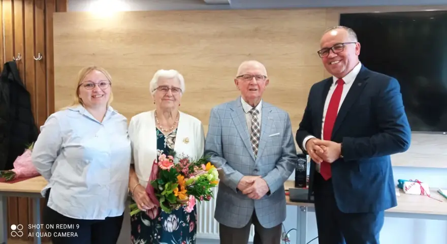 Para świętuje 65 rocznicę ślubu. Jubilaci z bukietem kwiatów, obok nich młodsza kobieta i mężczyzna w garniturze.