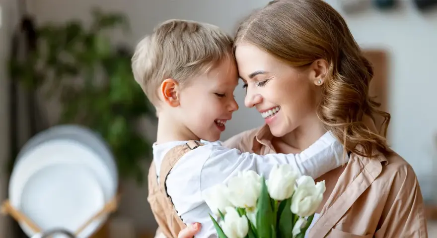 Uśmiechnięta mama i synek przytulają się, trzymając bukiet białych tulipanów. Idealny obrazek na Dzień Mamy.