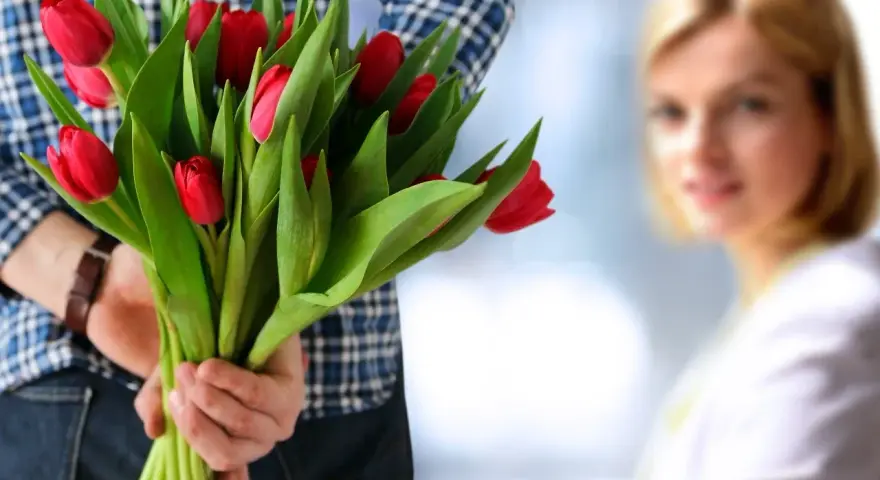 Mężczyzna z bukietem czerwonych tulipanów za plecami, zbliża się do kobiety.
