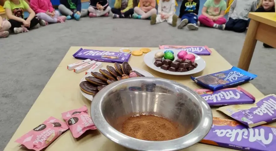 Dzieci czekają na słodkie pomysły na dzień czekolady. Na stole czekają czekolady Milka, Kinder i ciastka.
