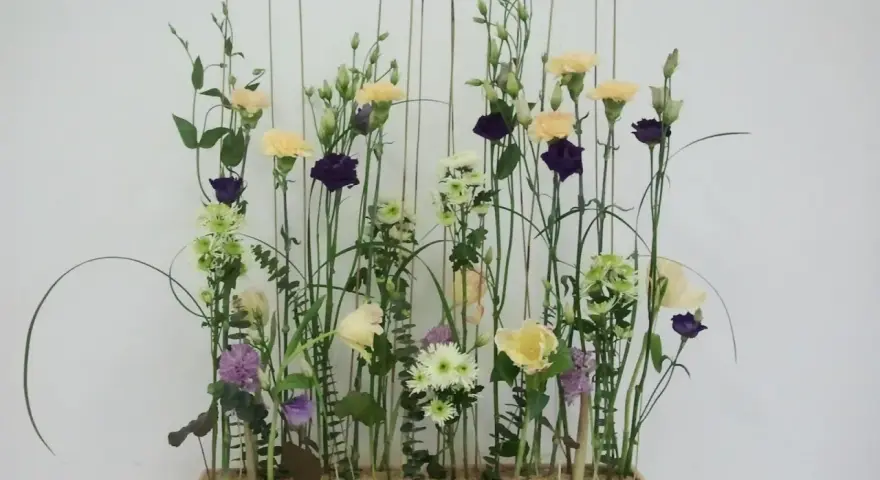 Kwiaty w pastelowych barwach i ciemnofioletowe akcenty, ułożone w stylu wegetatywnym we florystyce, tworzą lekki, naturalny bukiet.