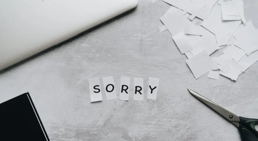 Litery wycięte z papieru układają się w napis "SORRY". Obok leżą nożyczki i stos białych skrawków, jakby ktoś tworzył piękny list na przeprosiny.