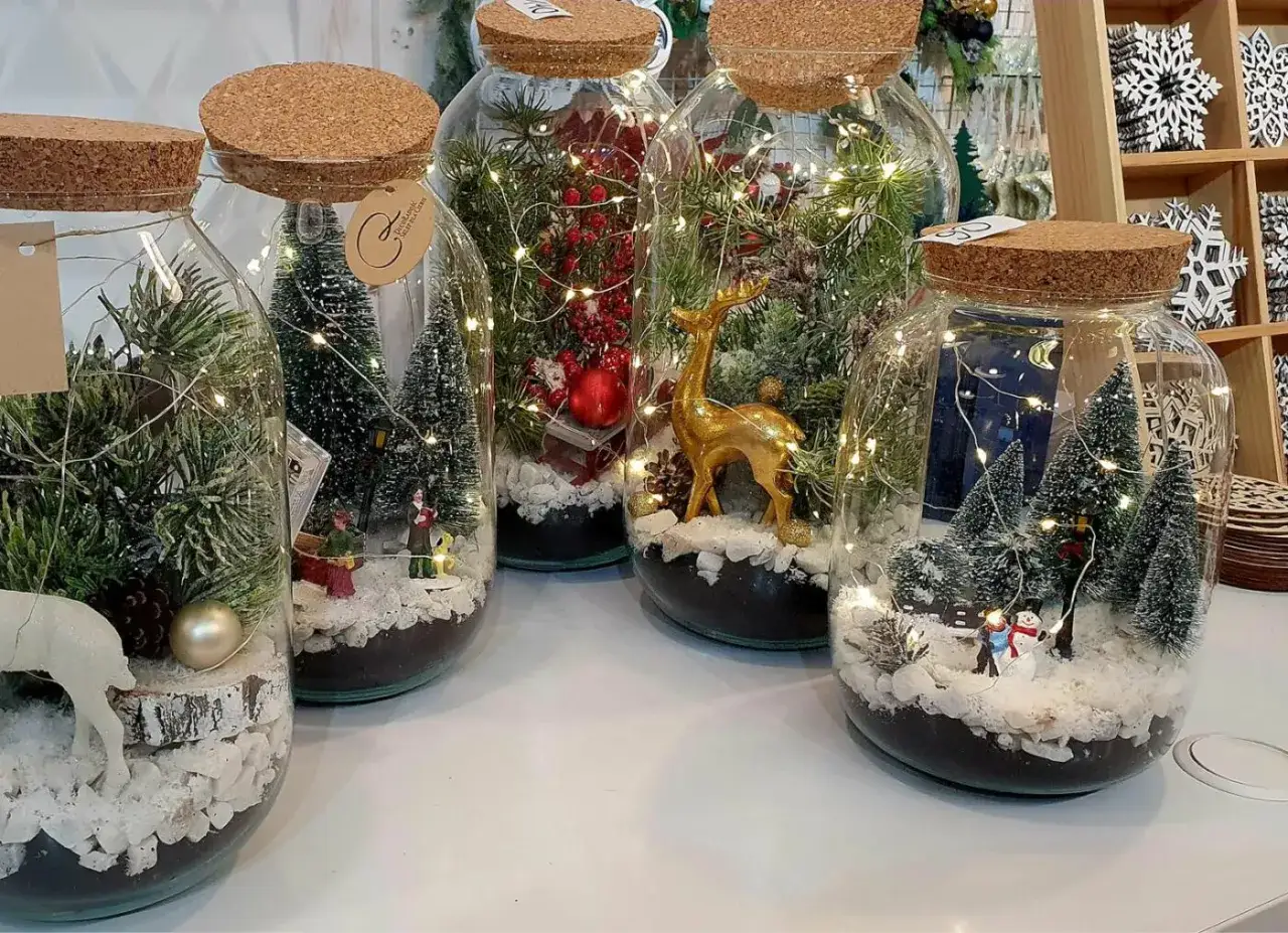 Świąteczne dekoracje DIY w słoikach: miniaturowe lasy, bałwanki i złoty jeleń, oświetlone lampkami.